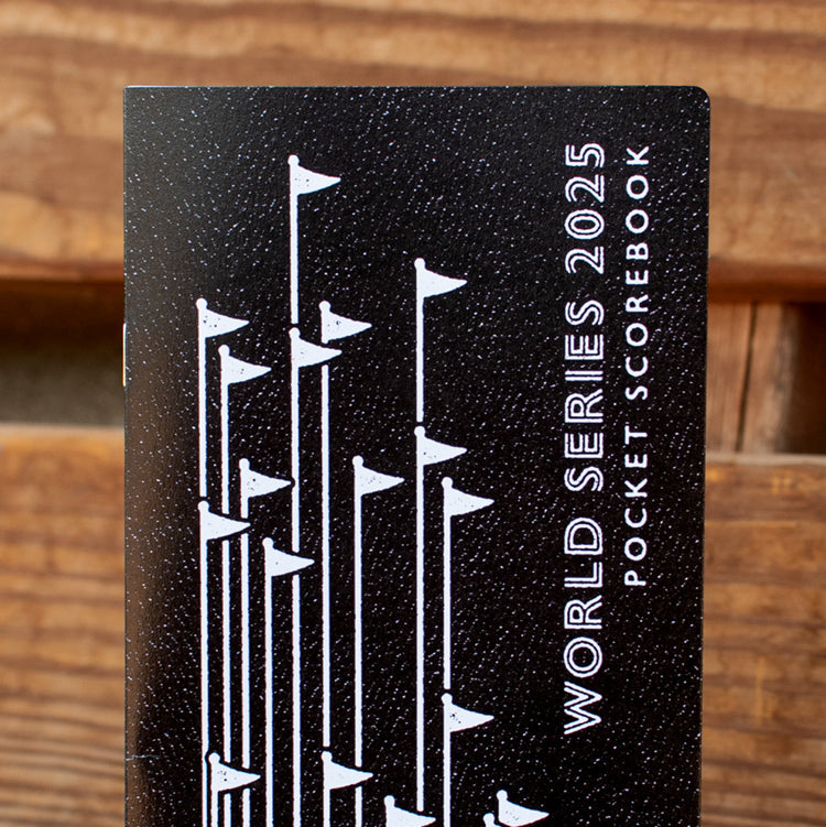 Black pocket scorebook with white text and design on a wooden background