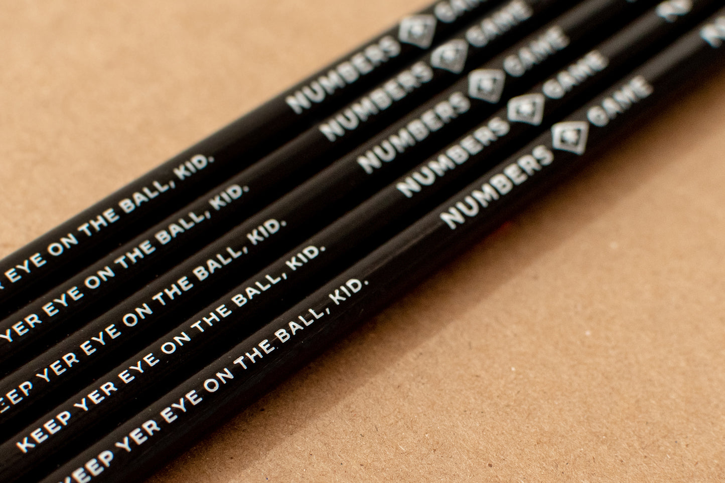 Numbers Game pencils are painted black and feature the Numbers Game brand logo and the phrase, "Keep yer eye on the ball, kid." printed in white.